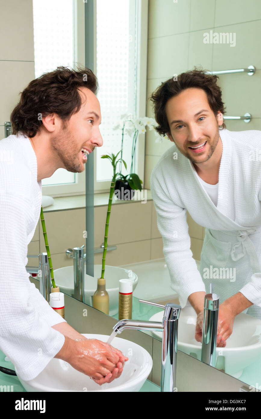 Young man in the hotel bathroom, suite, refreshing himself and washing the face at the sink Stock Photo