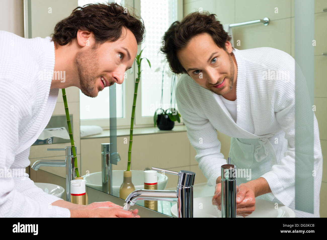 Young man in the hotel bathroom, refreshing himself and washing the face at the sink Stock Photo