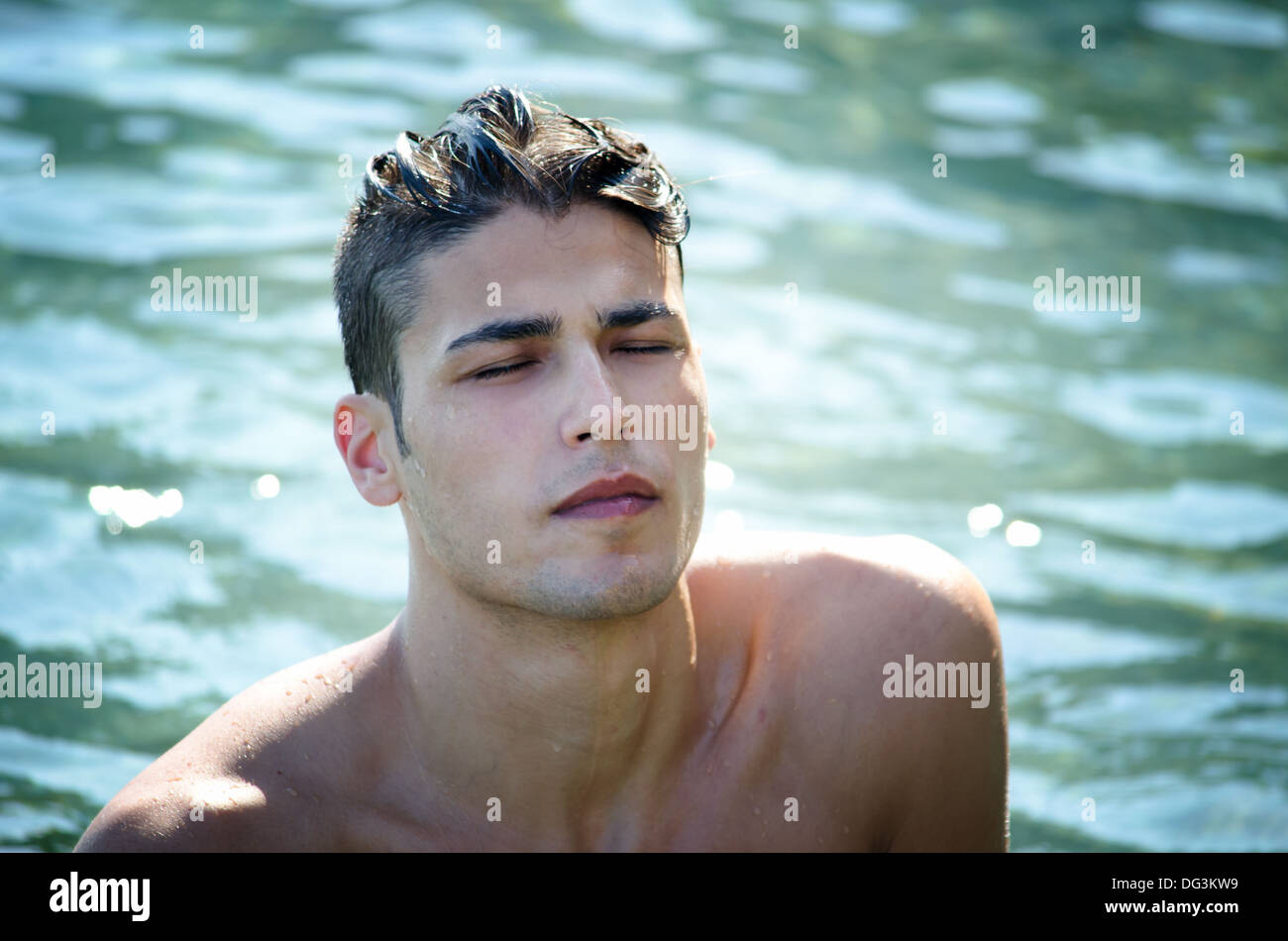 Handsome young man coming out of water with wet hair, eyes closed. Stock Photo