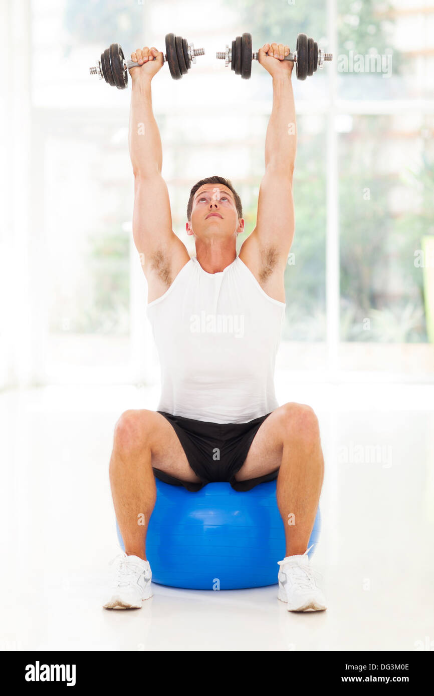 healthy man lifting up a dumbbells seated on fitness ball Stock Photo