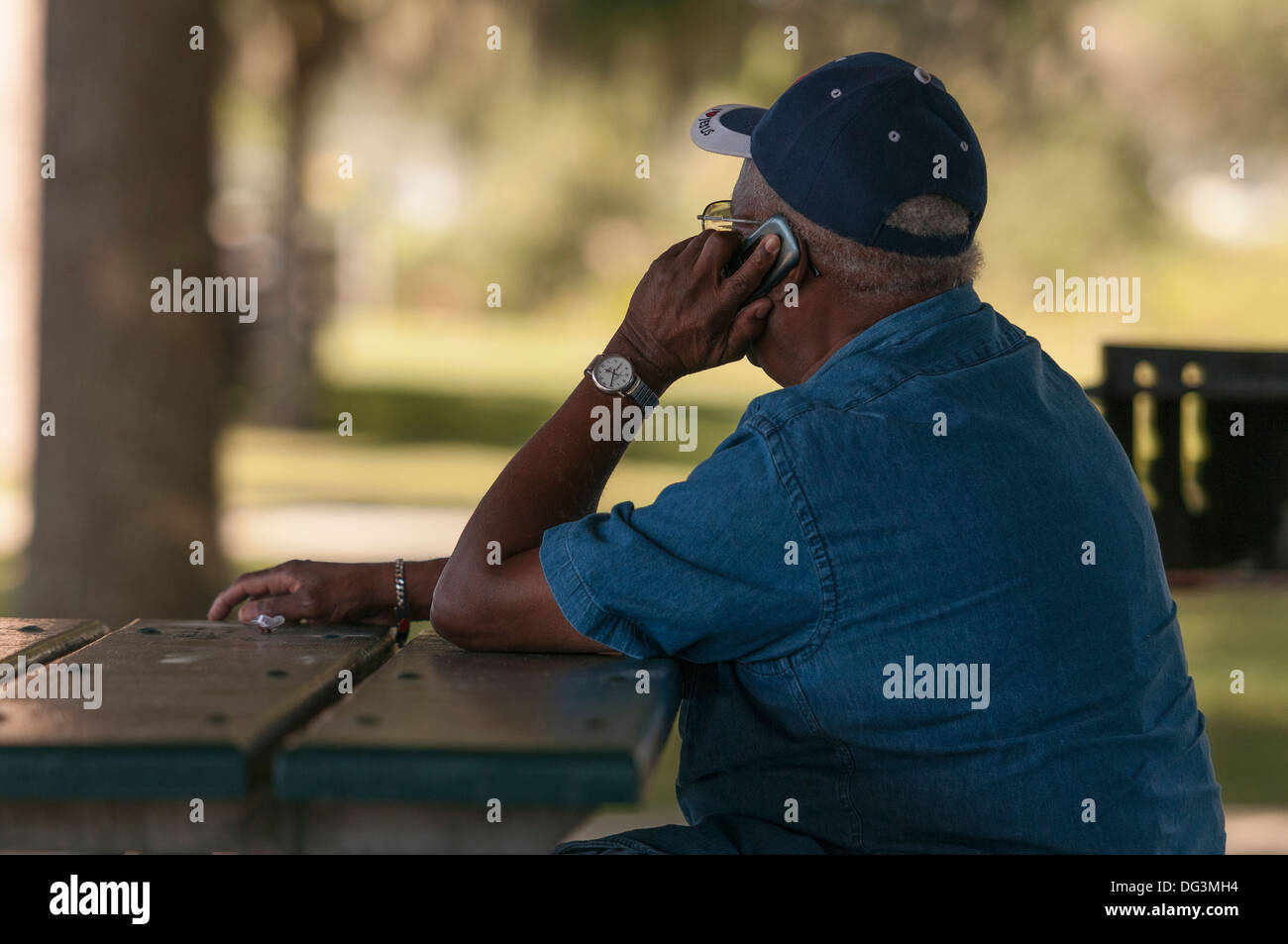 Man sitting at park picnic bench talking on cell phone Stock Photo