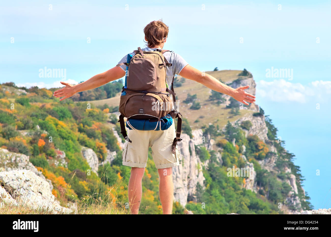 Man Traveler with backpack standing outdoor hands raised to the blue sky with mountains on background Freedom Stock Photo