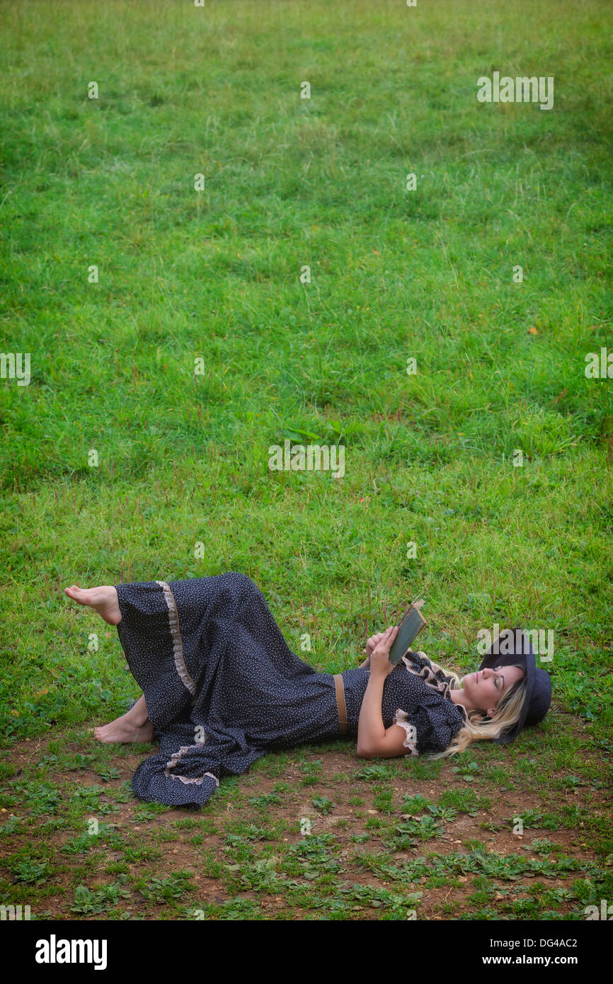 a woman in a romantic dress is lying on a meadow, reading a book Stock Photo