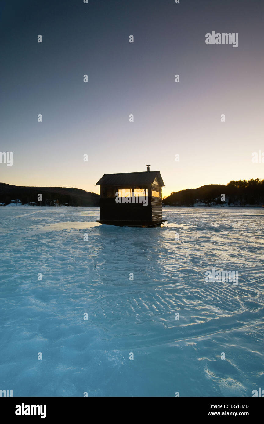 An icefishing shanty sitting on a frozen lake is sihouetted against