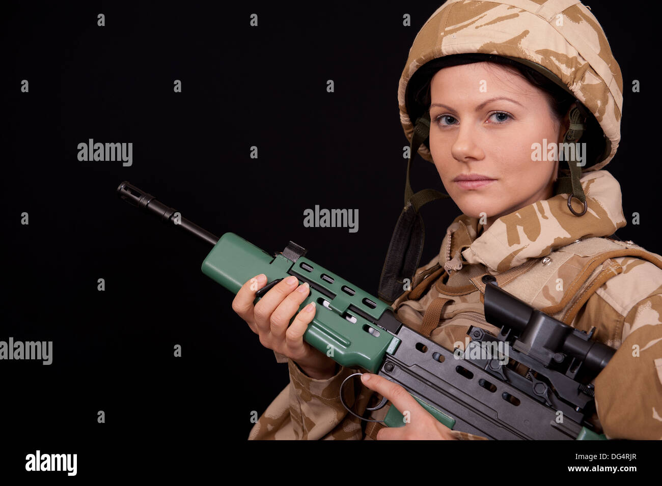 Female soldier holding an SA80 rifle, against a black background. She is wearing British Military desert camouflage uniform. Stock Photo