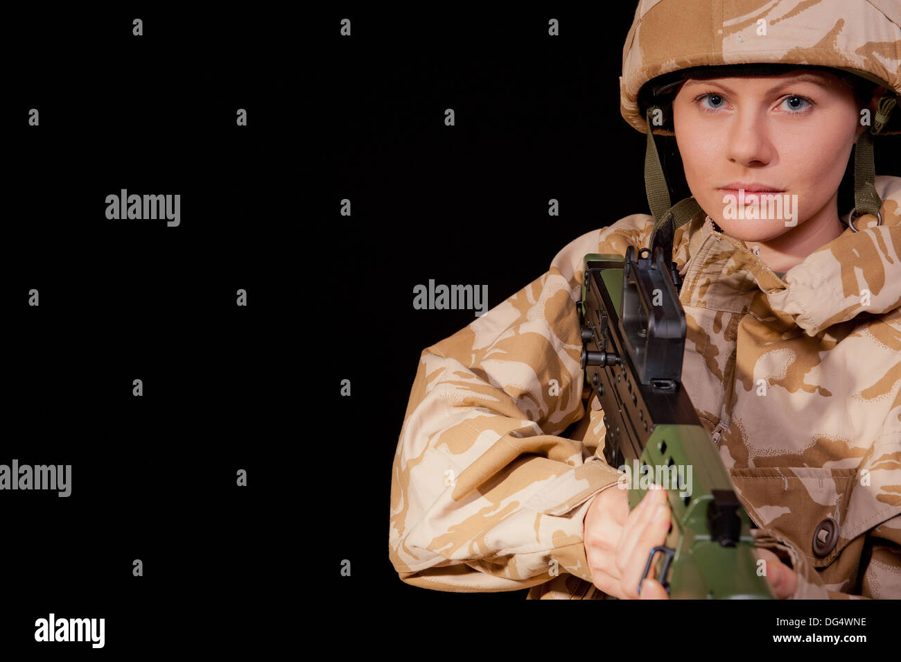 Female soldier holding an SA80 rifle, against a black background. She is wearing British Military desert camouflage uniform. Stock Photo