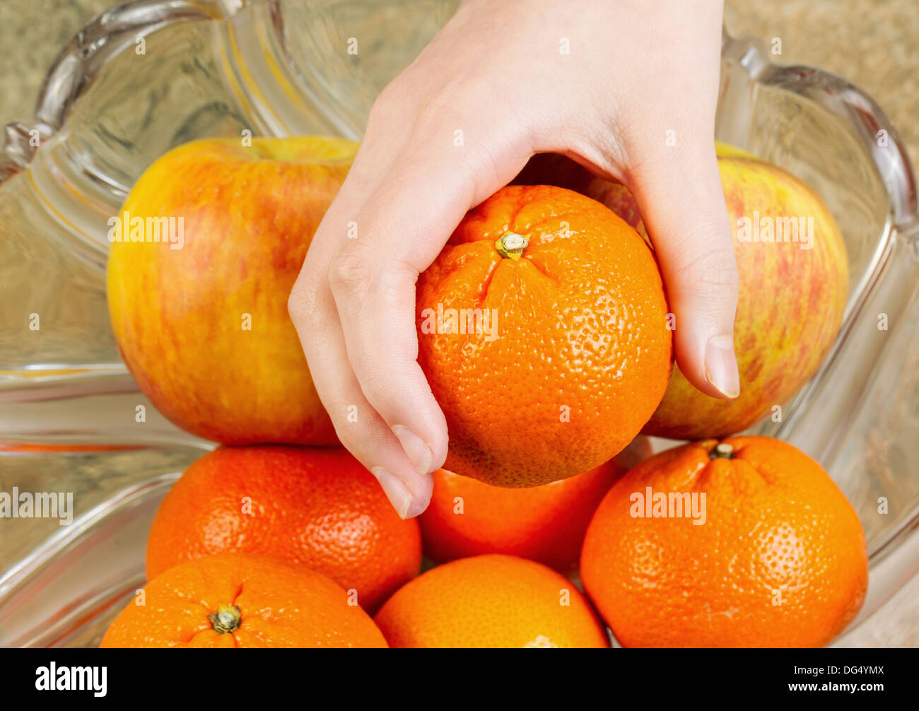 Photo of female hand selecting fresh ripe orange fruit from glass bowl ...