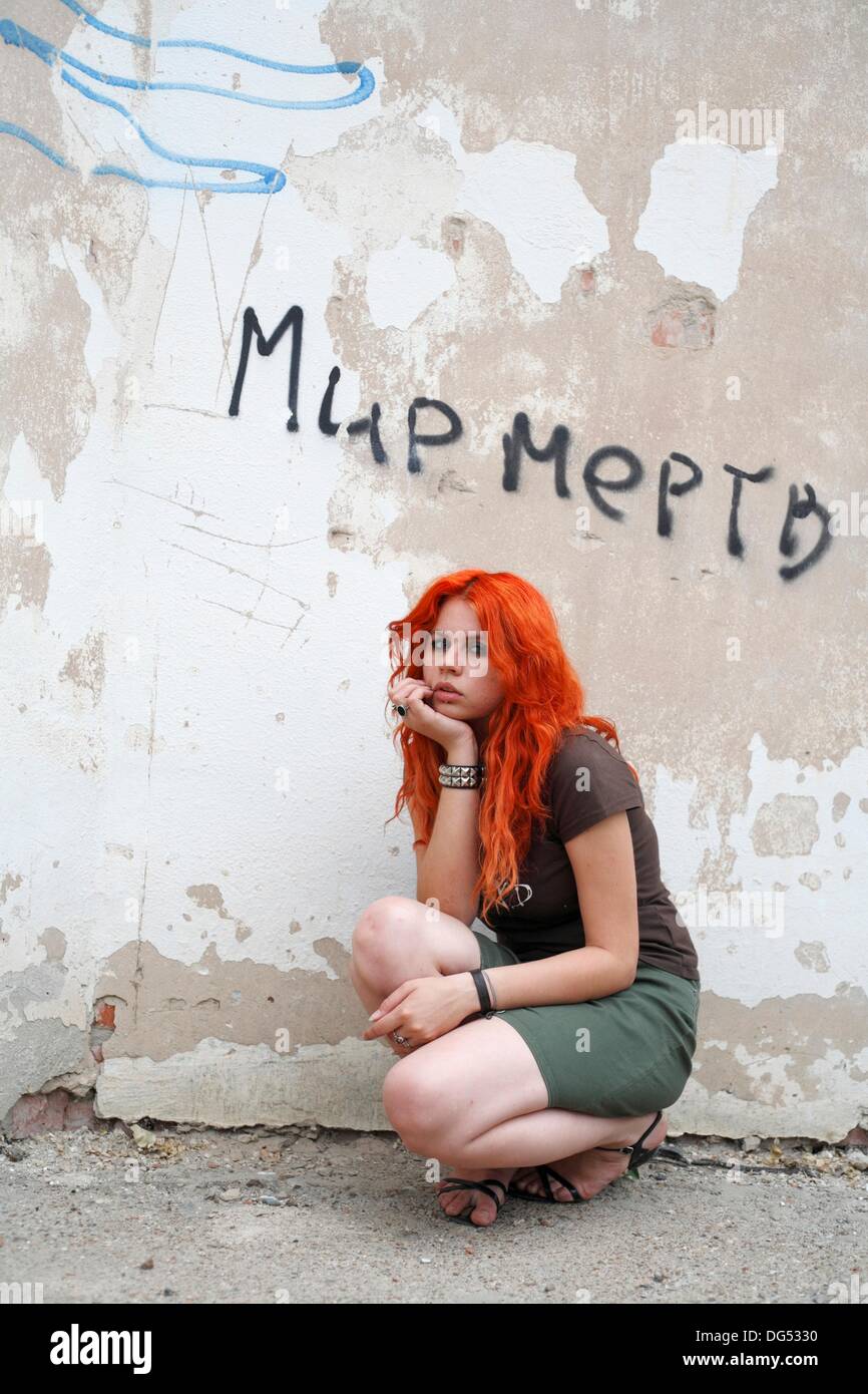 pretty redhead girl against obsolete wall with words in Russian ´World is dead´ Stock Photo