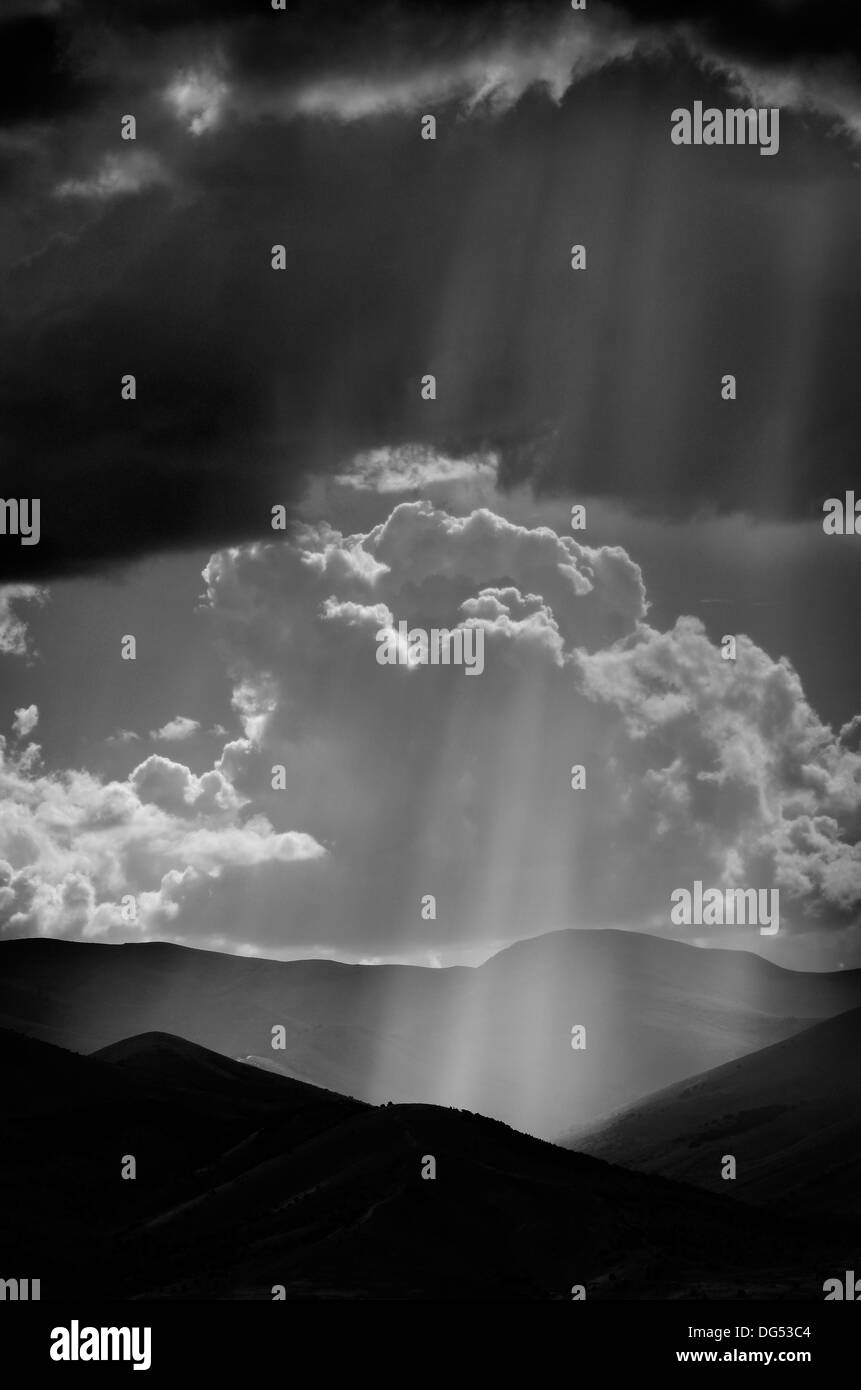 Sunlight rays from clouds falling on dark mountain range Stock Photo