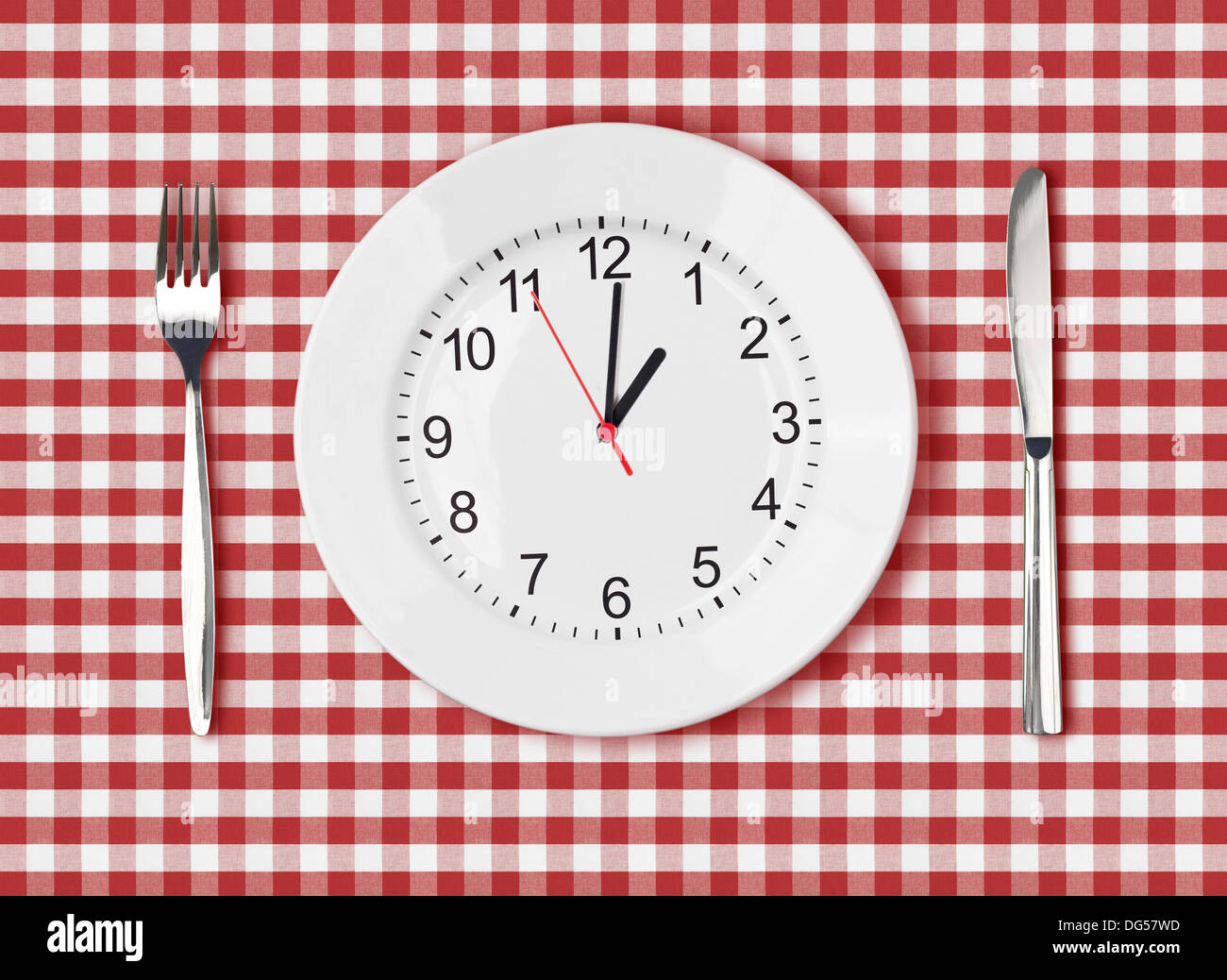 Knife, white plate with clock face and fork on red picnic table cloth Stock Photo