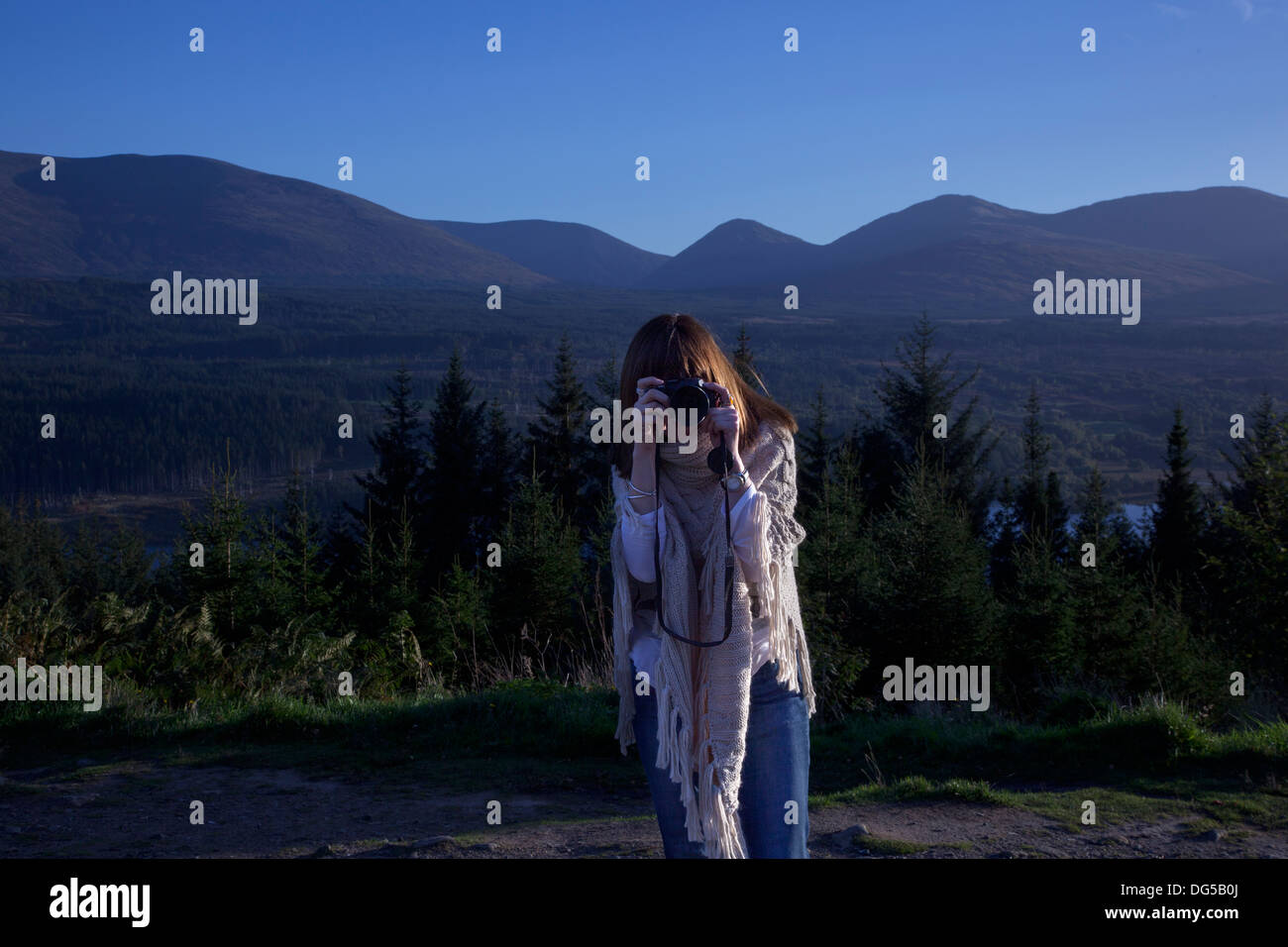 Woman taking a photograph, aiming the camera front on. Set by a beautiful Scottish Loch. Invergarry Loch. Stock Photo
