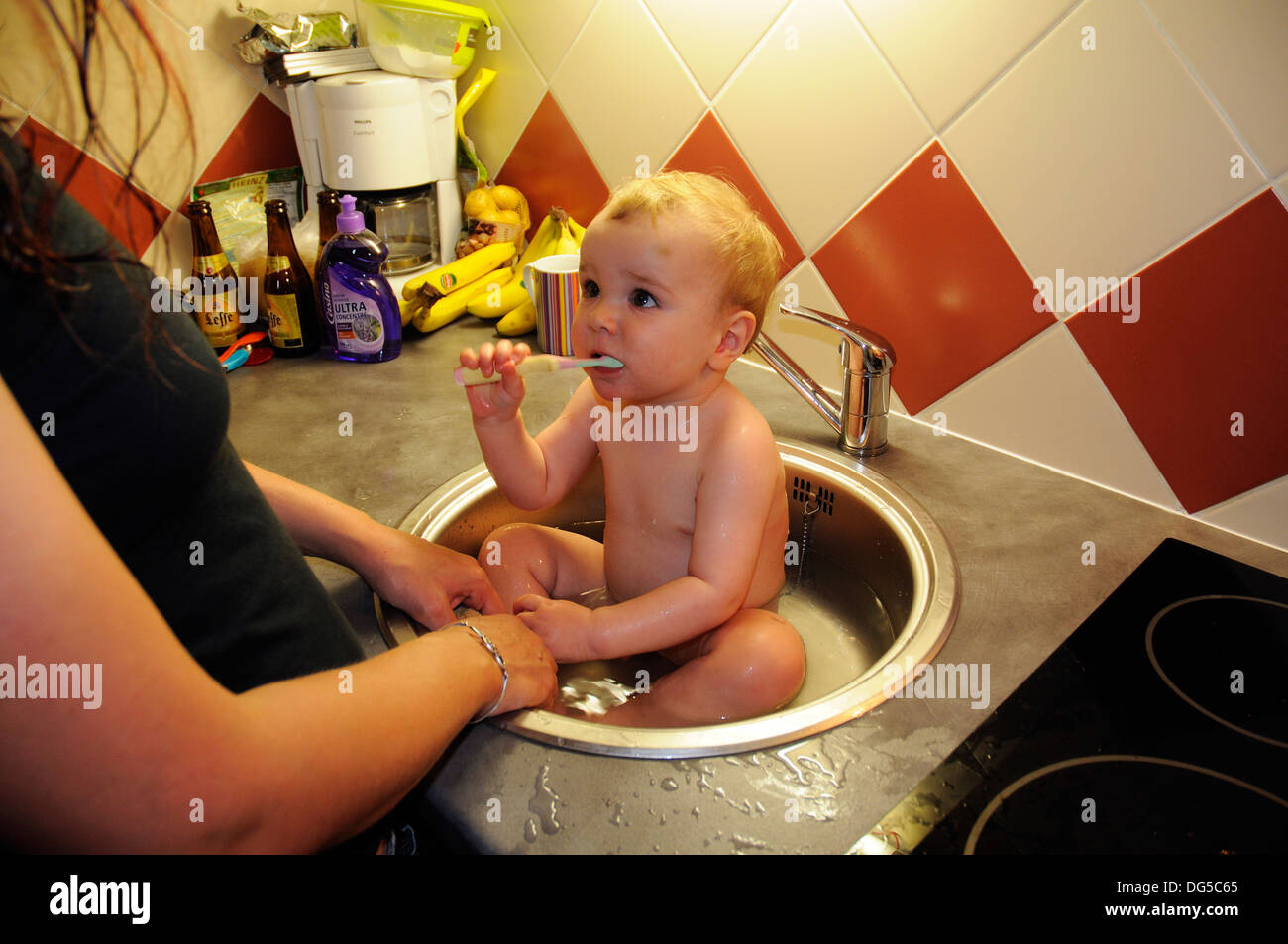 A baby having his bath and scrubbing his teeth in the kitchen sink Stock Photo