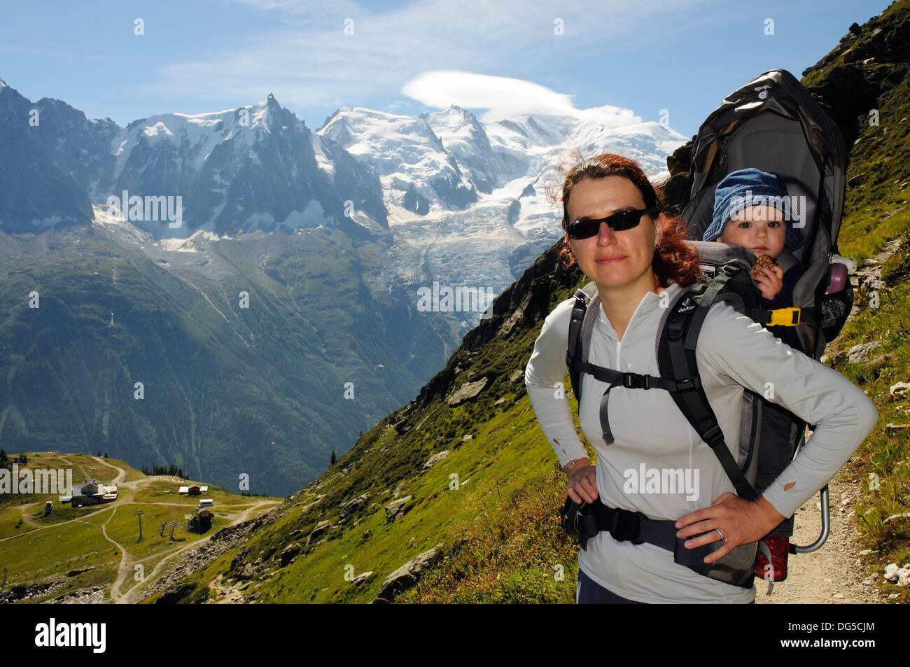 A mother hiking in the French alps carrying her child in a baby carrier with Mont Blanc behind Stock Photo