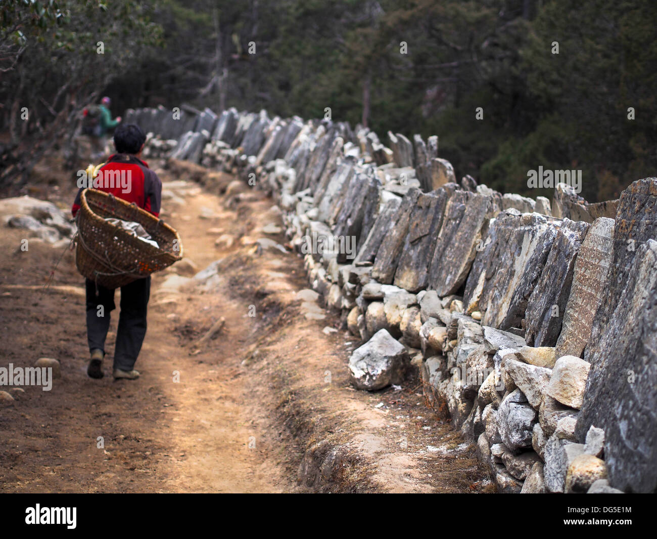A Sherpa porter walking next to Mani stones on the trail to Everest Base Camp in Nepal. Stock Photo