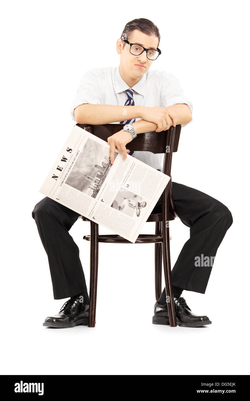 Disappointed young businessperson sitting on a wooden chair and holding a newspaper Stock Photo