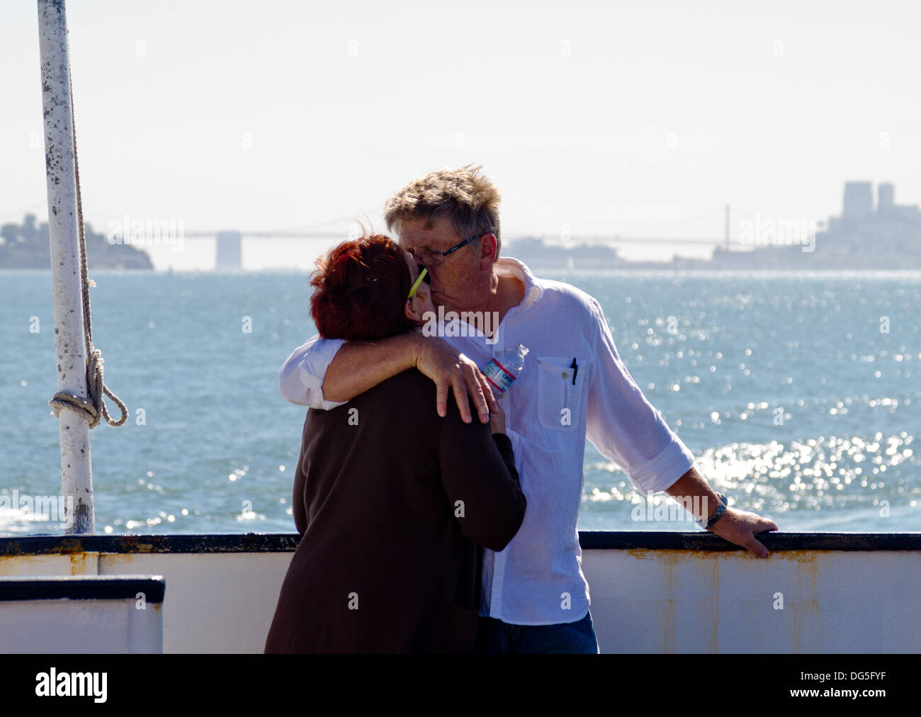 Middle-aged couple passionately kissing aboard a ferry boat on San Francisco Bay with the city and bridge in background. Stock Photo