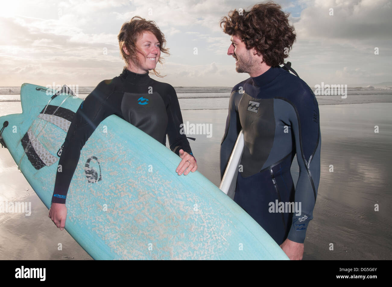 couple standing on beach with surfboards, one has a Gopro camera attached to surfboard Stock Photo