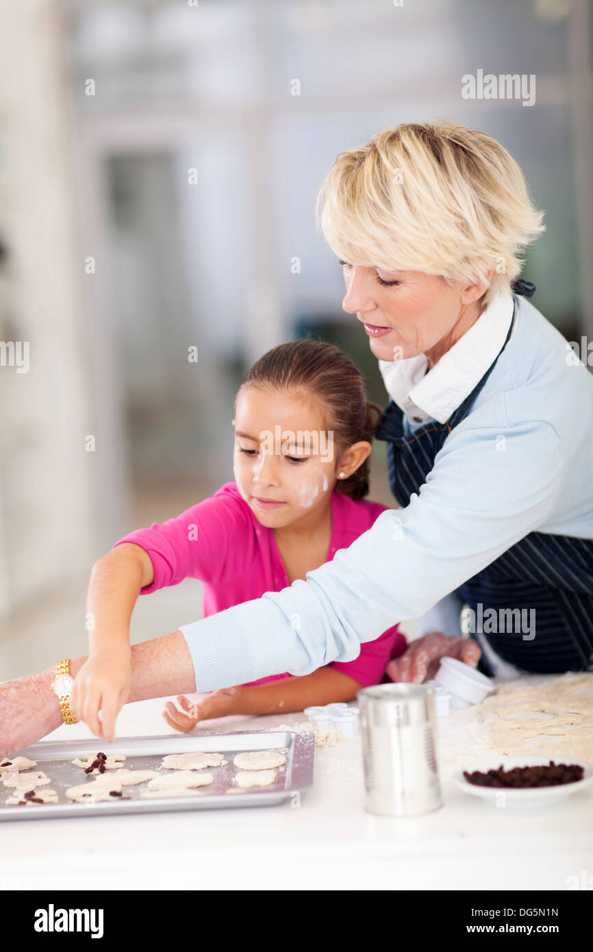 pretty little girl with grandmother baking cookies together at home ...