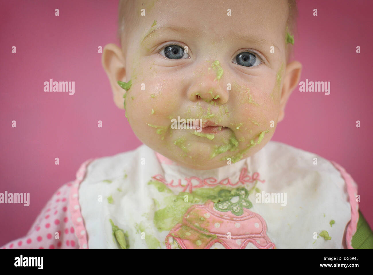 Baby girl sat in a high hi chair eating avocado Stock Photo