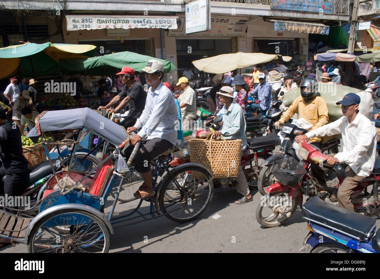 Several cyclo drivers are peddling along with motorcycle drivers on a busy street in Phnom Penh, Cambodia. Stock Photo