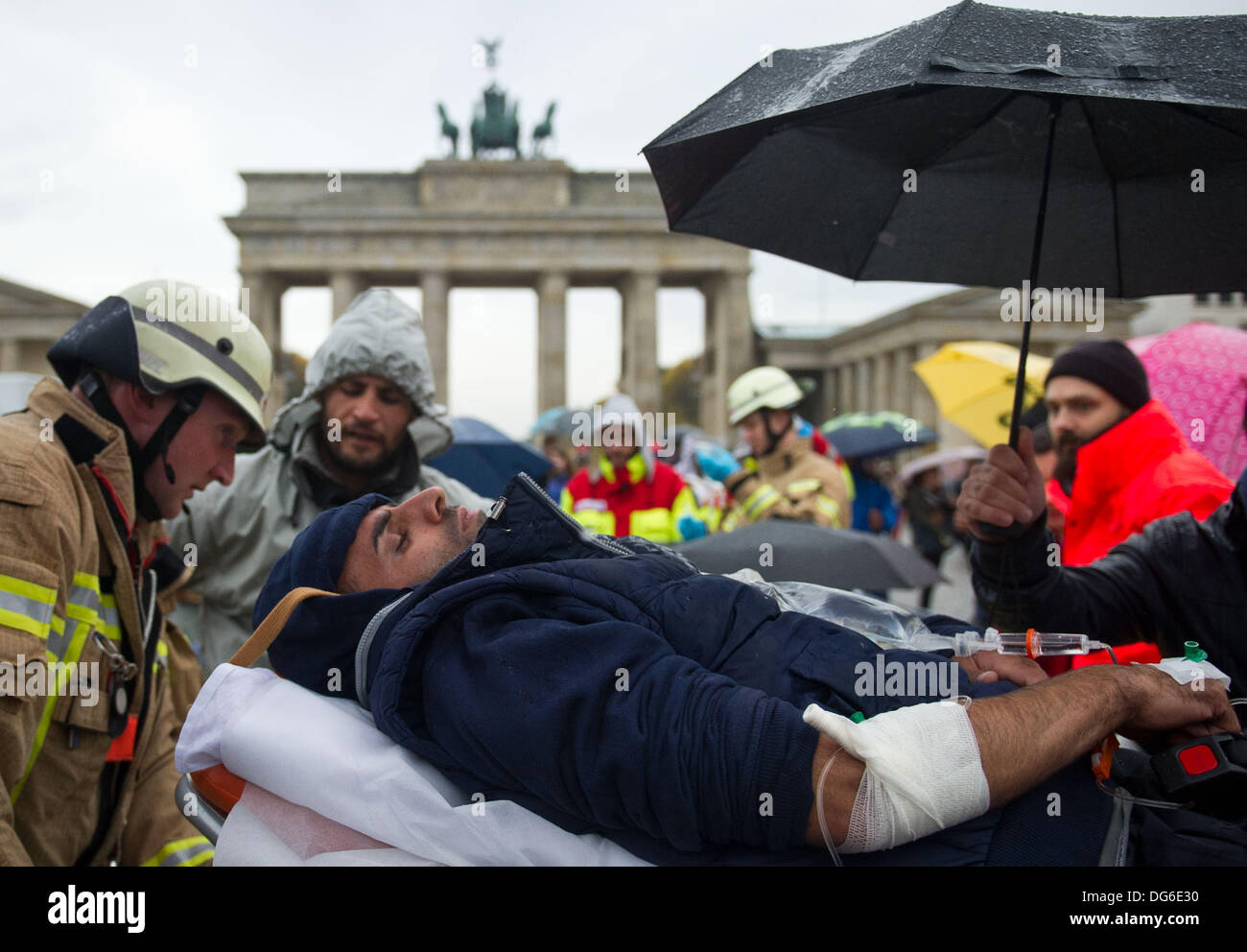 Berlin, Germany. 15th Oct, 2013. Rescue workers take a refugee on a stretcher to a hospital on Pariser Platz in Berlin, Germany, 15 October 2013. Three refugees had to be taken to hospital because of their poor state of health. The refugees have been on hunger strike since 09 October 2013. Photo: OLE SPATA/dpa/Alamy Live News Stock Photo