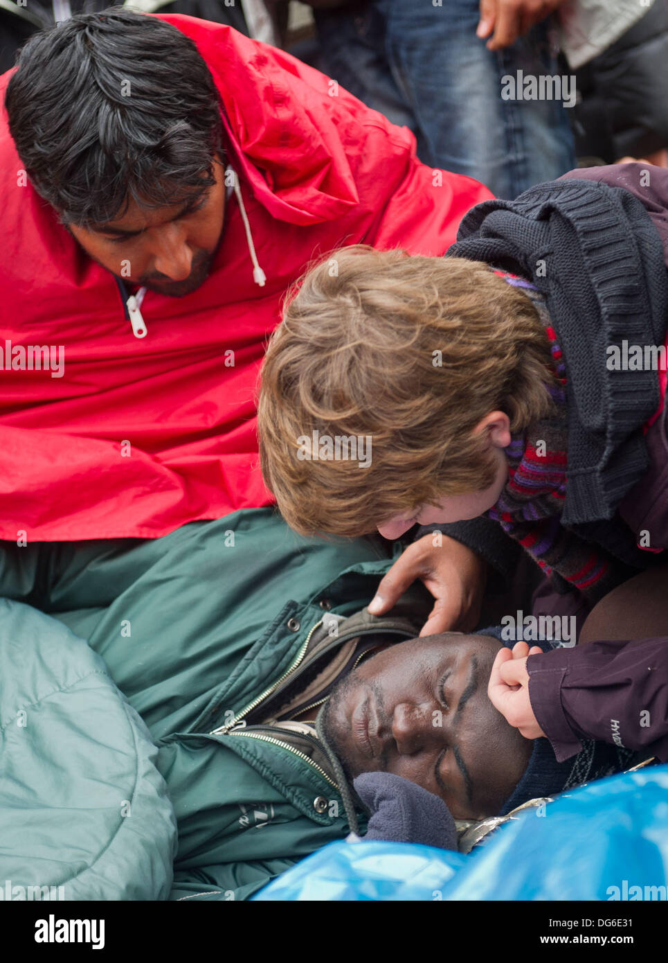 Berlin, Germany. 15th Oct, 2013. A refugee lies on the ground as his comrades take care of him on Pariser Platz in Berlin, Germany, 15 October 2013. Three refugees had to be taken to hospital because of their poor state of health. The refugees have been on hunger strike since 09 October 2013. Photo: OLE SPATA/dpa/Alamy Live News Stock Photo