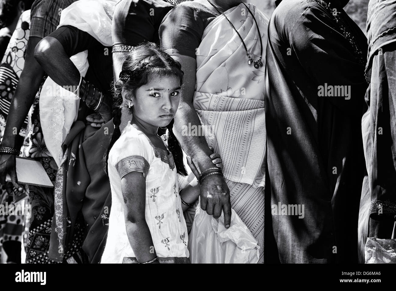 Unhappy indian girl waiting in line with women at Sathya Sai Baba mobile outreach hospital. Andhra Pradesh, India. Monochrome Stock Photo