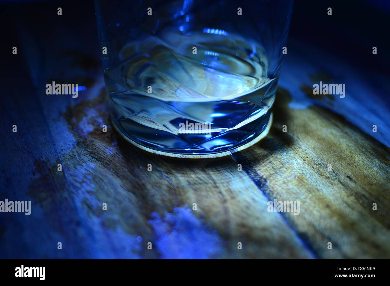 Glass of water on wooden table with spillage stain at night Stock Photo