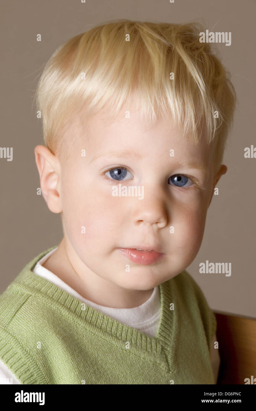 A blonde-hair, blue-eyed two year old boy looks straight at the camera. He  is wearing a white t-shirt and green jumper Stock Photo - Alamy