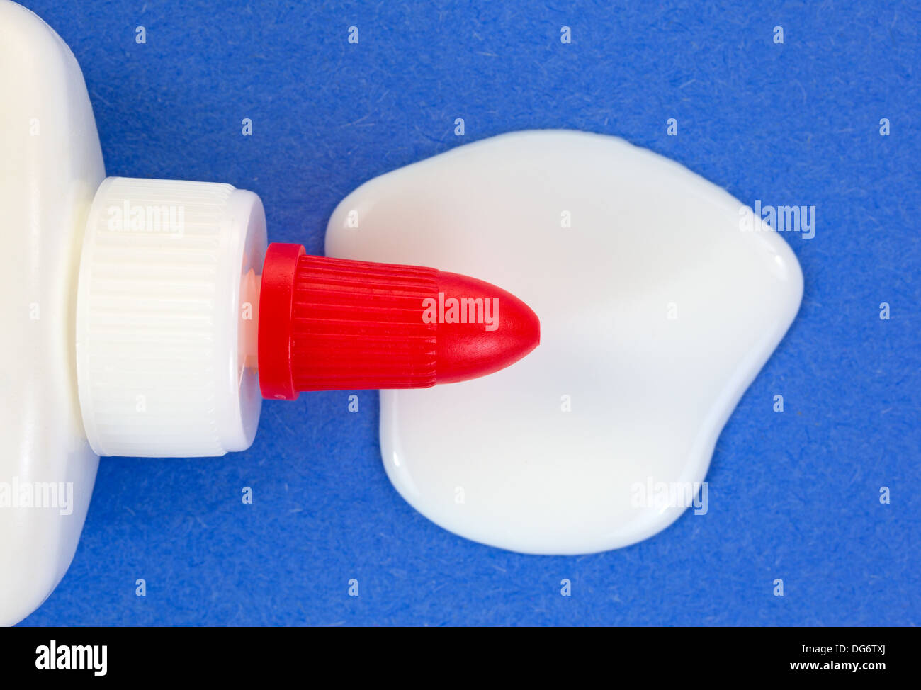 A close view of white glue that has spilled on to a piece of blue craft paper with the red top of the bottle above the spill. Stock Photo