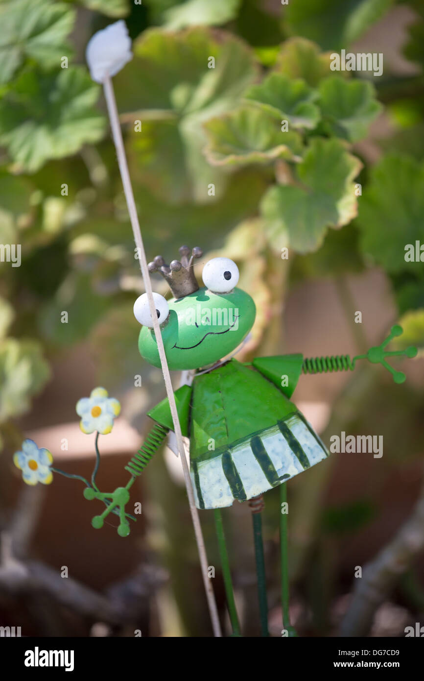Close up of a tinny funny hand-made frog with a silver crown, hang up in a tomato-plant. Stock Photo