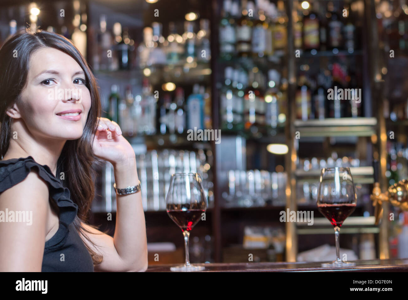 Beautiful young elegant brunette woman seated at a bar counter in an upmarket in a hotel, club or restaurant Stock Photo