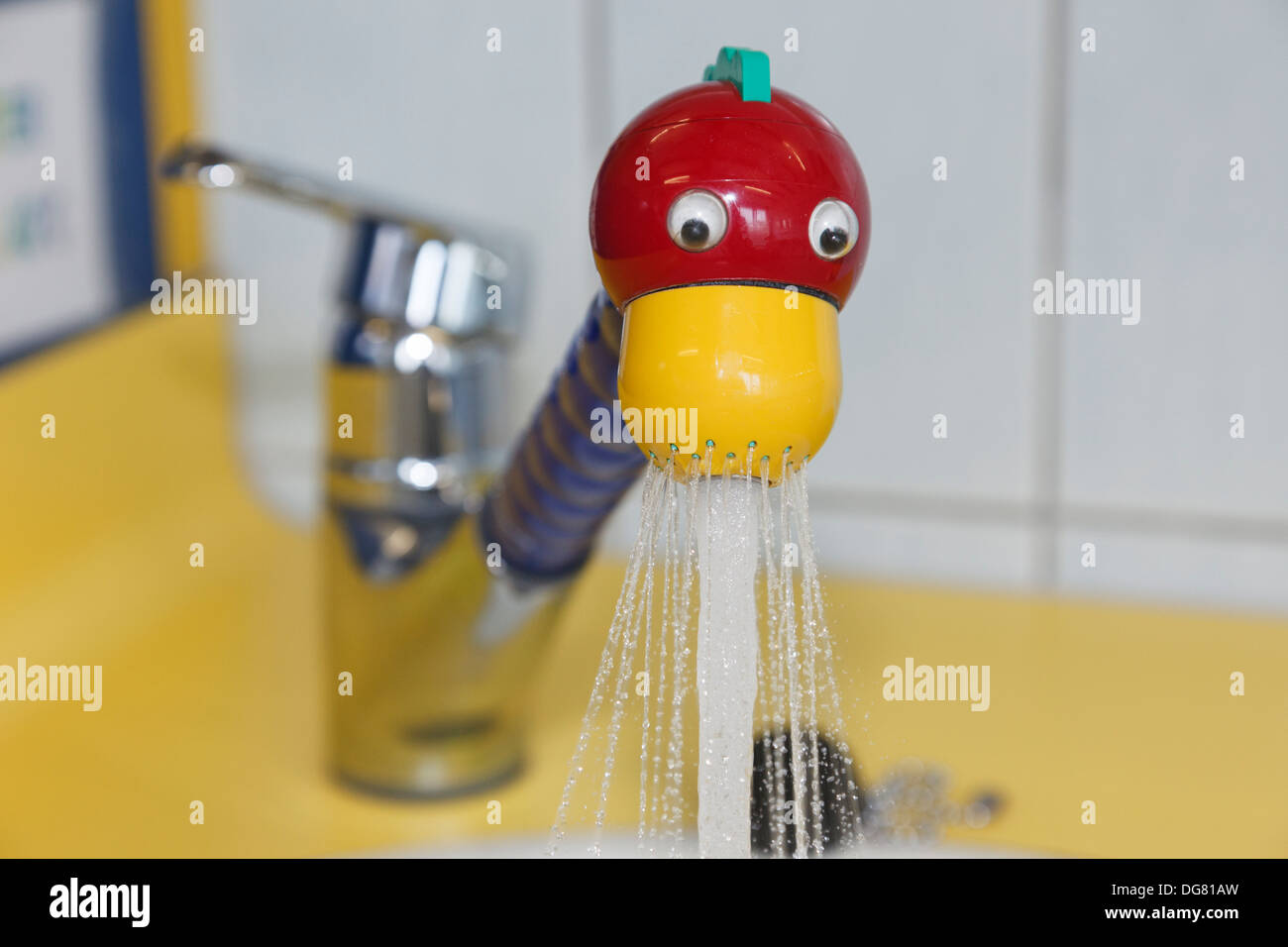 Tap in a red and yellow novelty fun duck's head design switched on spraying water into a wash basin in a children's washroom Stock Photo