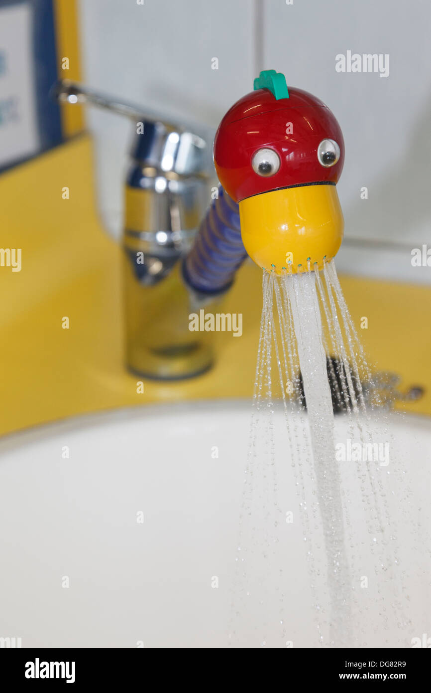 Tap in a red and yellow novelty fun duck's head design switched on spraying water into a wash basin in a children's washroom Stock Photo