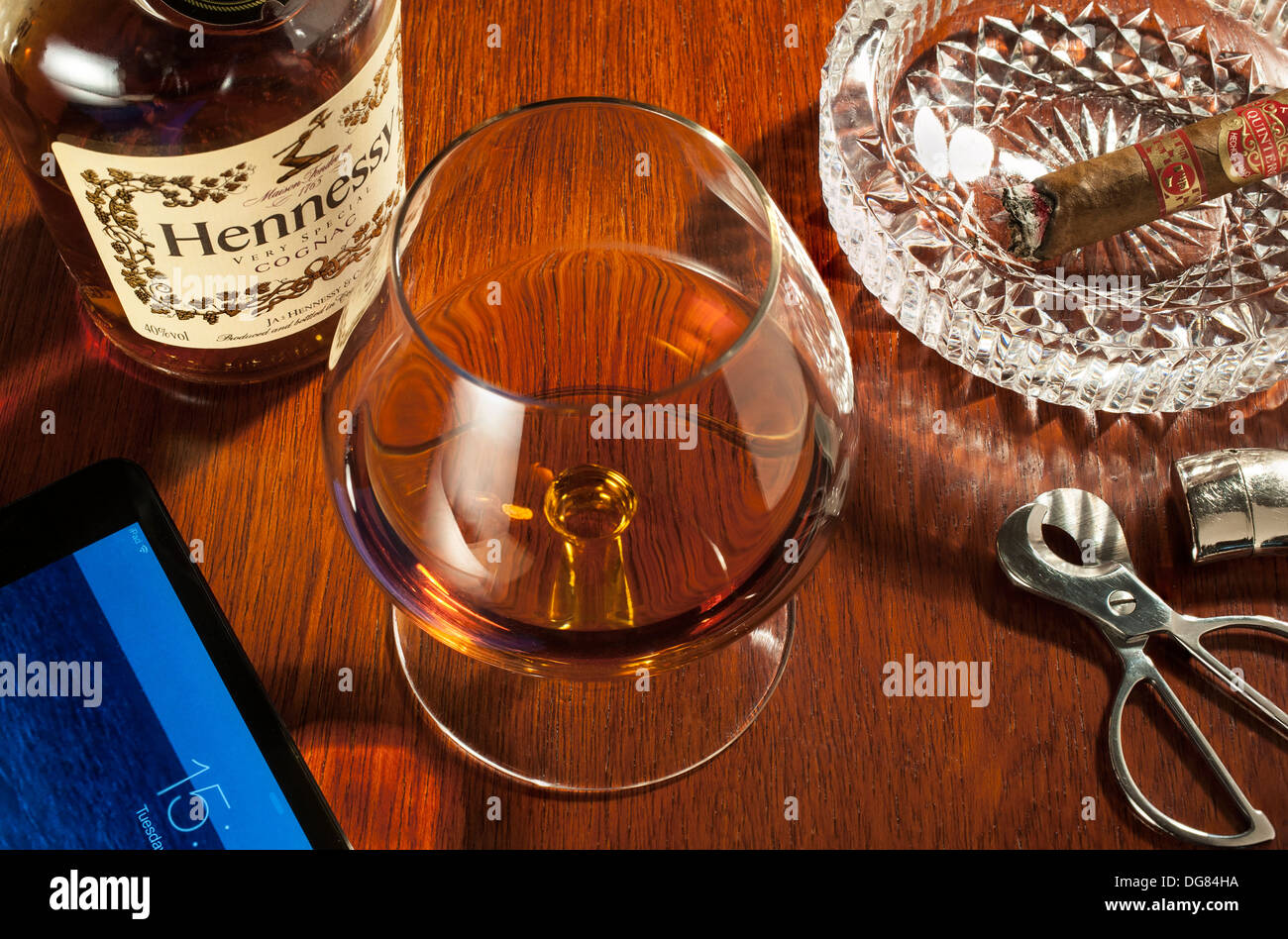 Brandy and cigars - A snifter glass of Hennessy brandy with a part smoked cigar in ashtray and an iPad Stock Photo