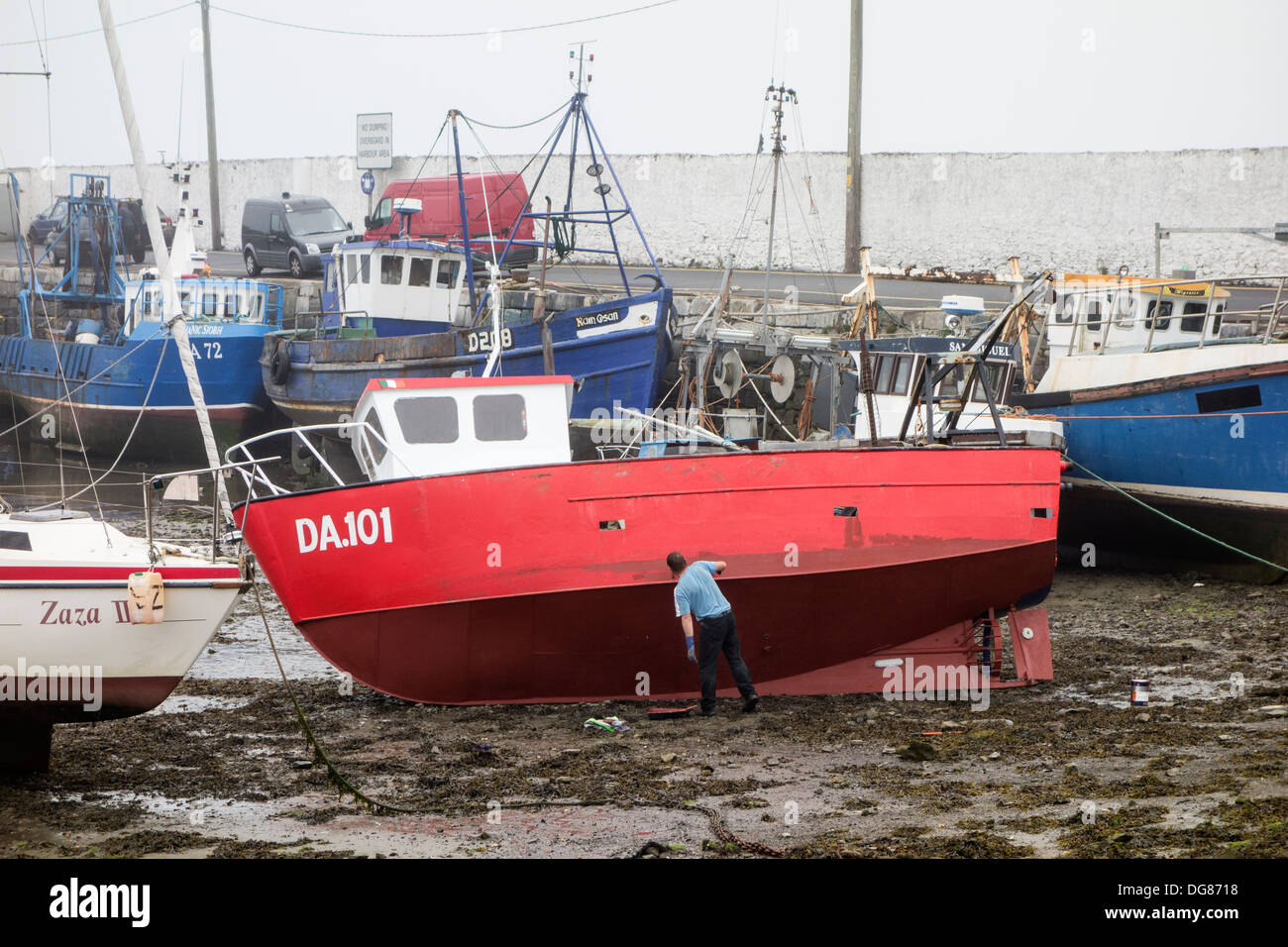 Painting the hull of a fishing boat while tide is out in the harbour - Skerries, County Dublin, Ireland Stock Photo