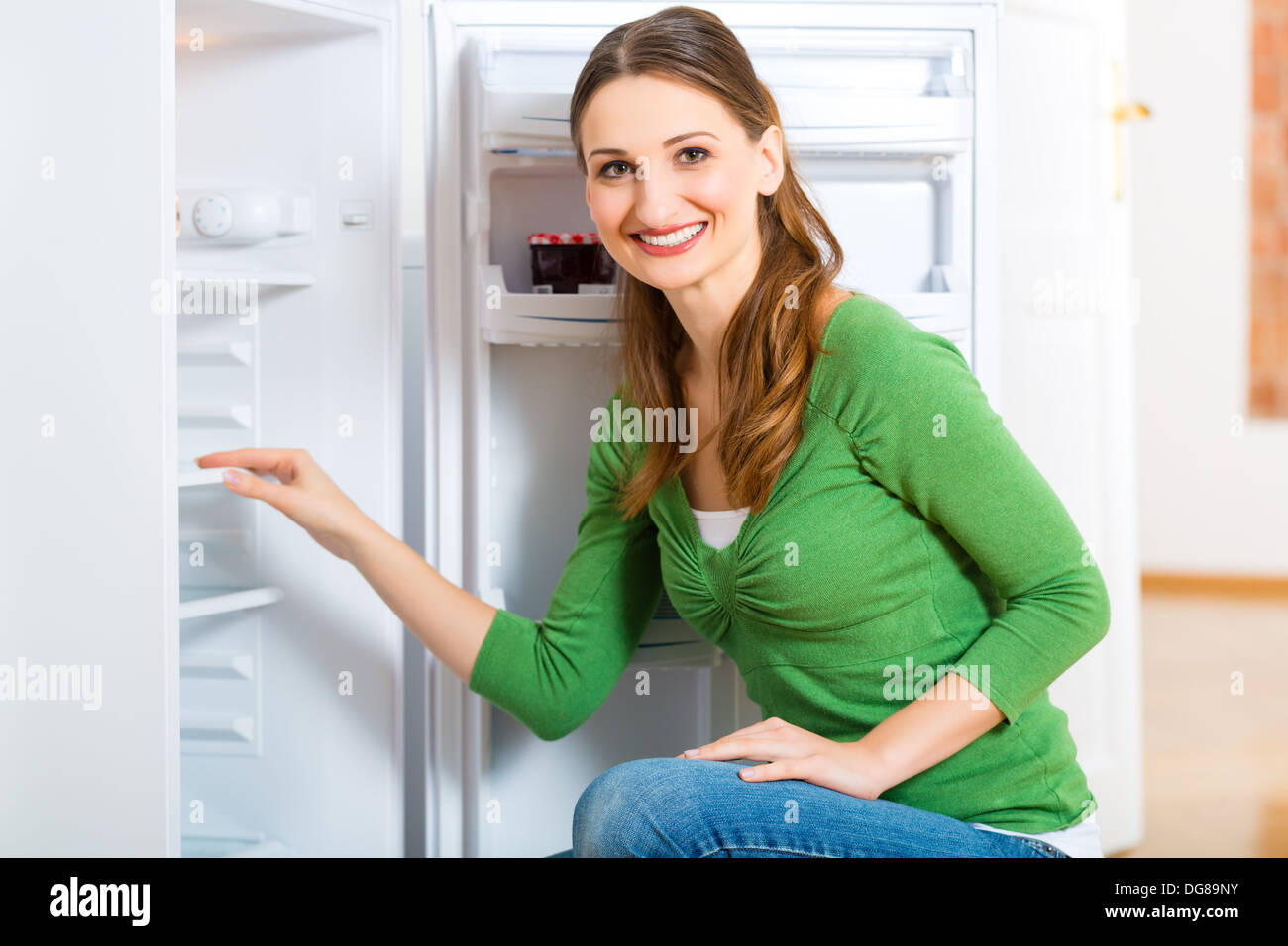 Young woman or housekeeper defrosts the refrigerator and wipes in clean Stock Photo
