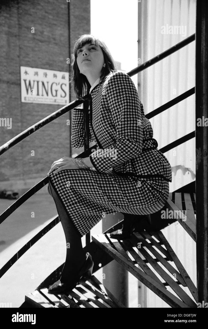 B&W fashion shot showing a young woman sitting in a spiral staircase. Stock Photo