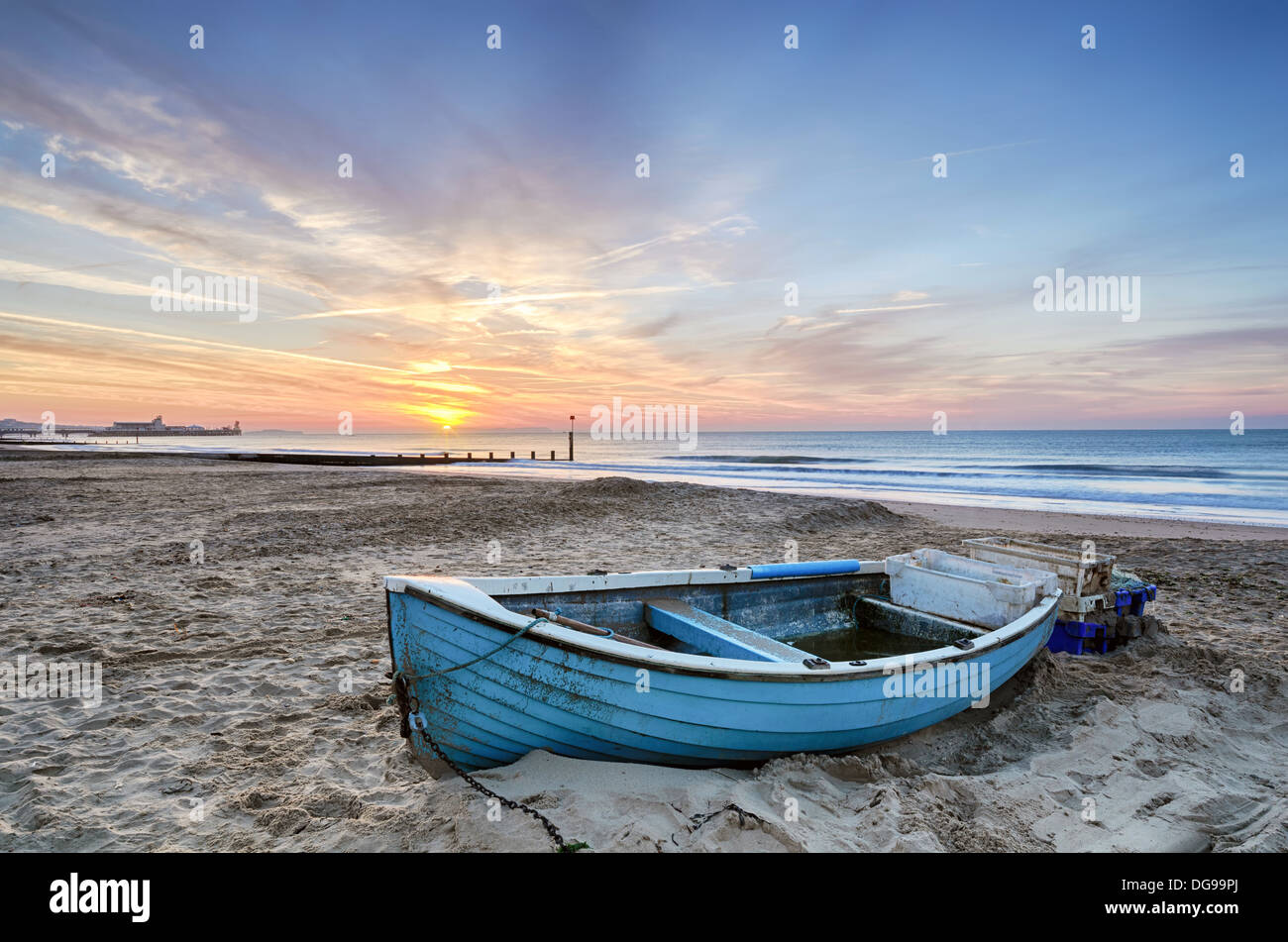 Turquoise blue fishing boat at sunrise on Bournemouth beach with pier in far distance Stock Photo
