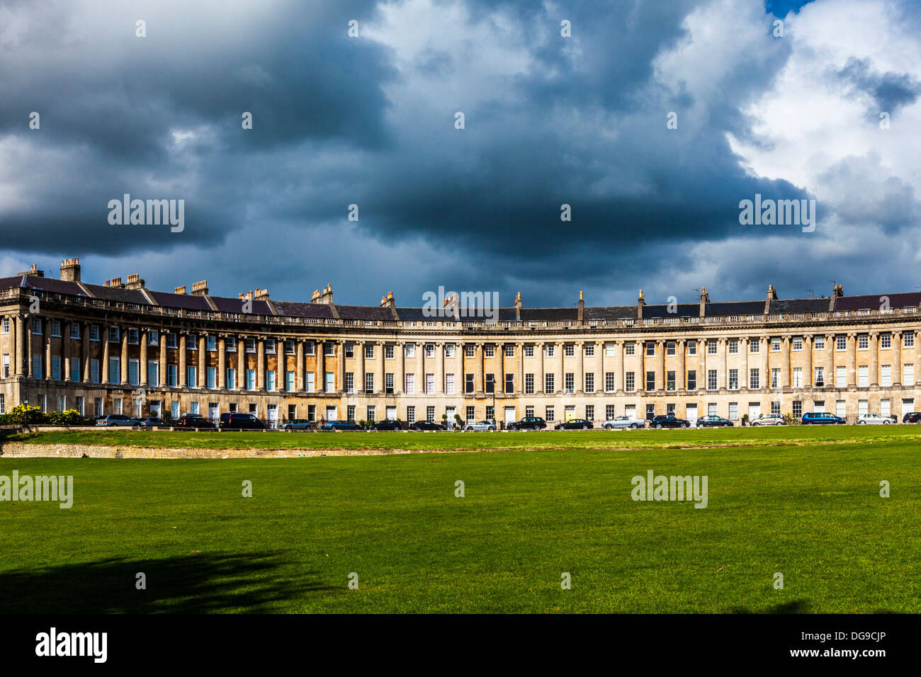 The sweeping sunlit Georgian facade of terraced houses in The Royal Crescent, Bath under lowering storm clouds. Stock Photo