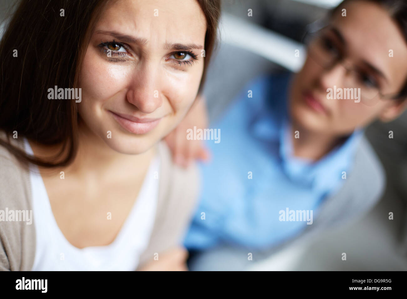 Crying girl looking at camera with her psychiatrist on background Stock Photo