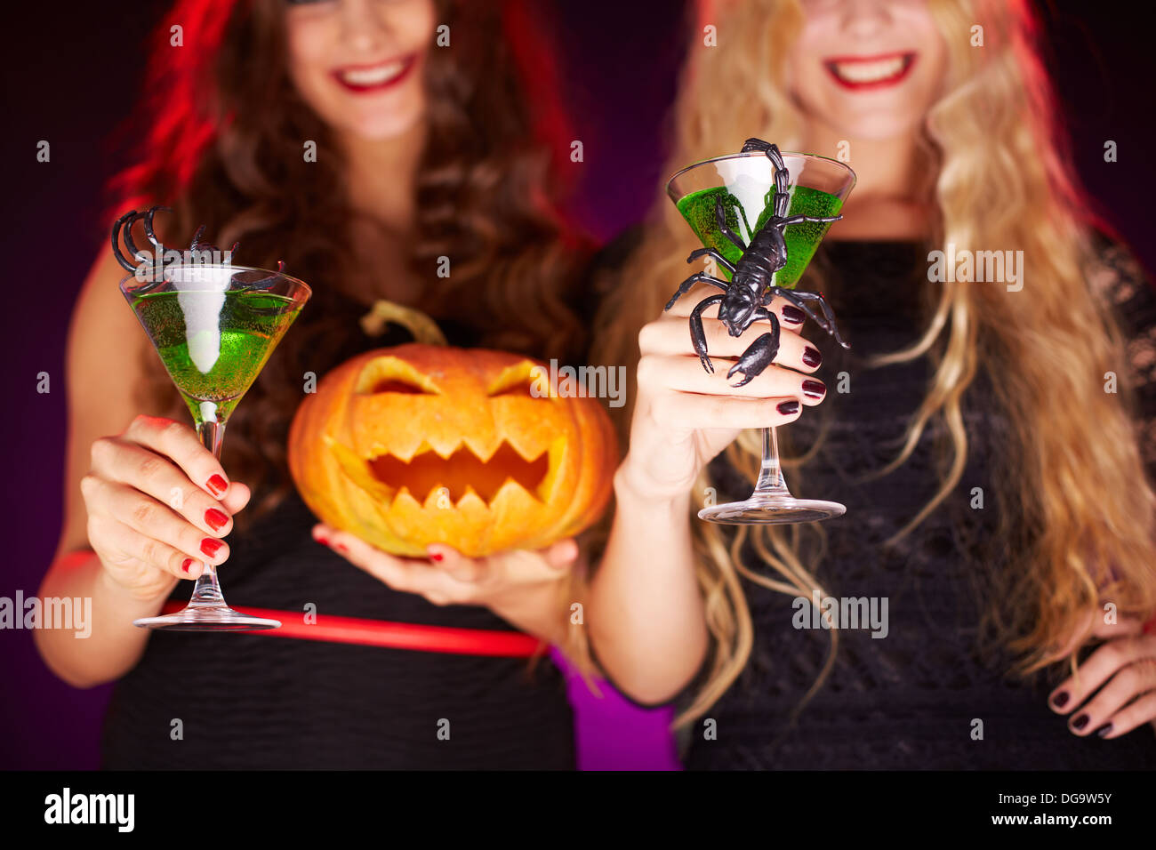 Photo of carved Halloween pumpkin and cocktails with scorpions held by females Stock Photo