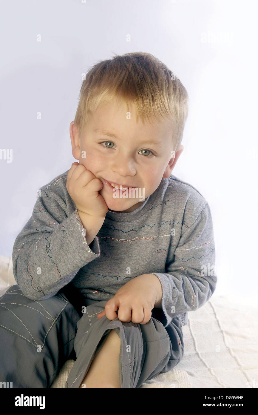 3 year old boy, smiling into camera sitting on the floor in studio