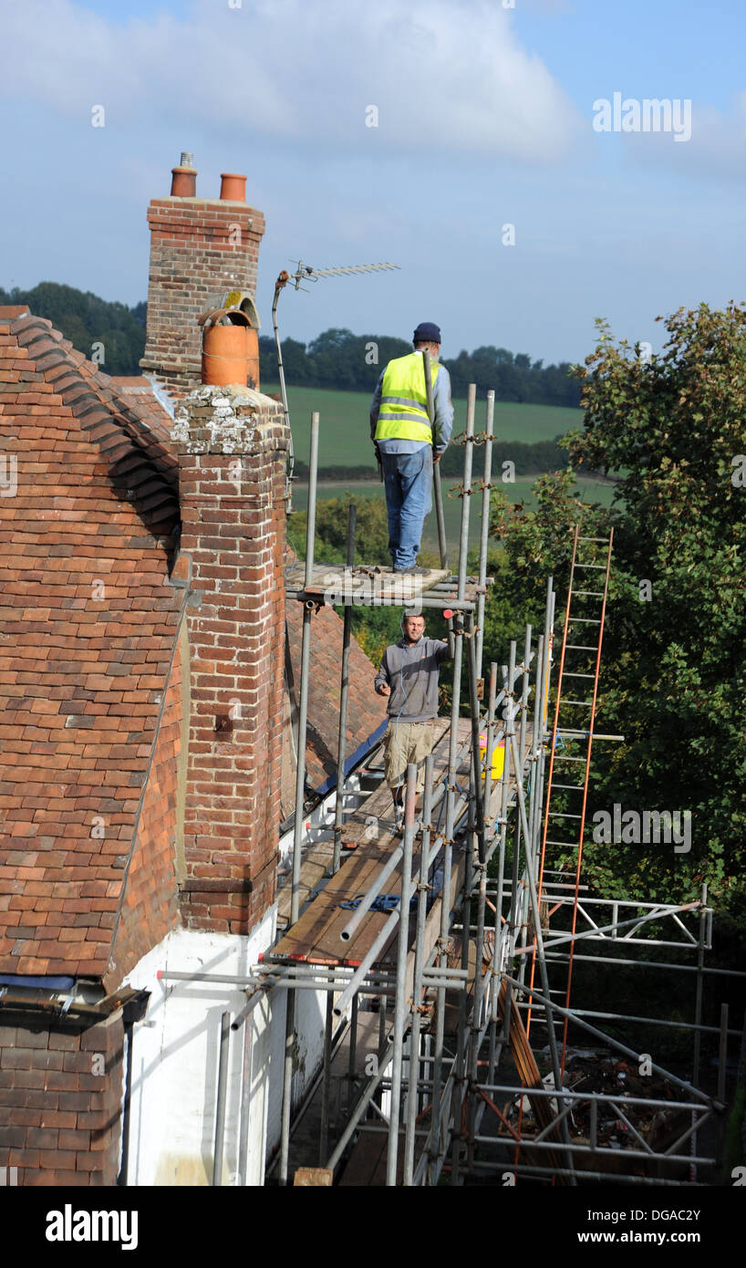 Builders working on scaffolding repairing roof on old historic house in Battle High Street Sussex UK Stock Photo