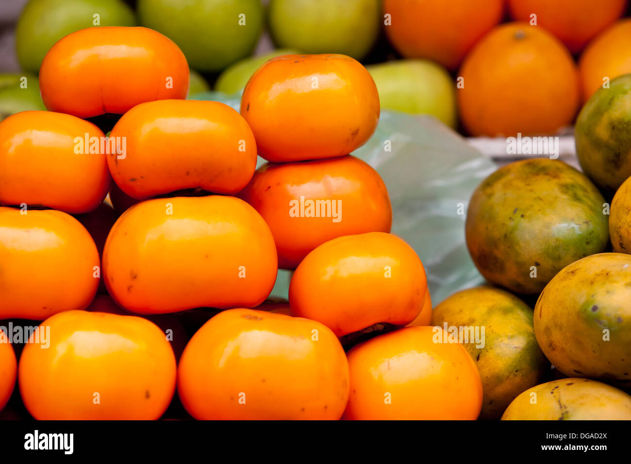 A pile of fresh persimmon fruit is displayed on a produce stand on a local street market stall in Siem Reap, Cambodia Stock Photo