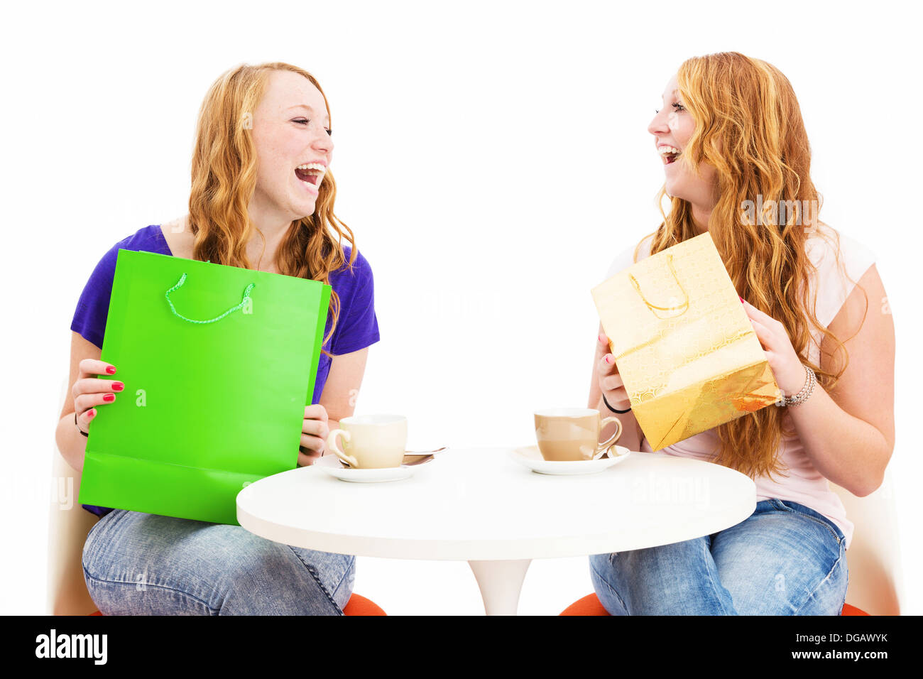 two happy laughing women with shopping bags sitting at a coffee table on white background Stock Photo