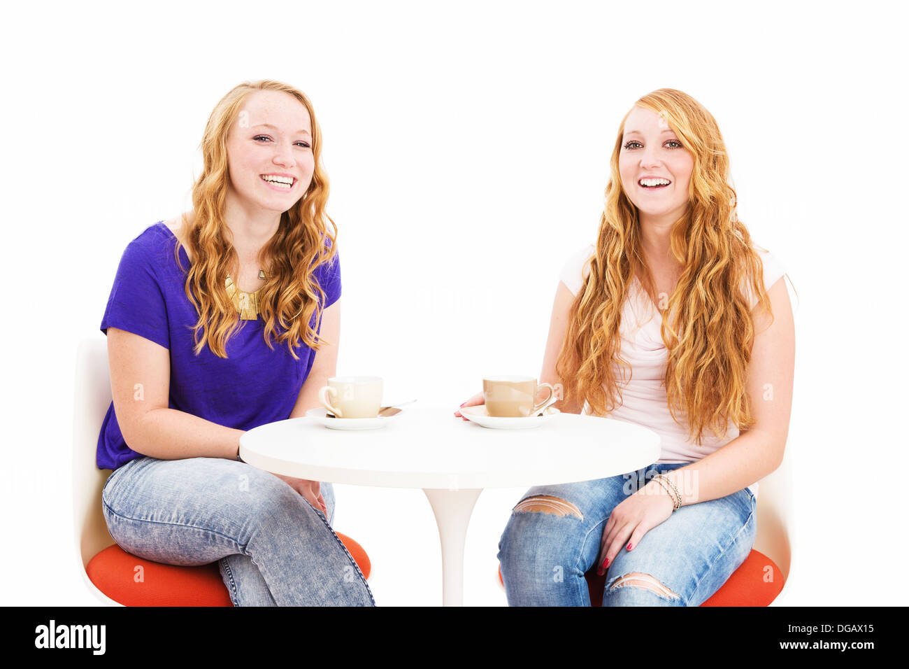 two laughing redhead women sitting at a coffee table on white background Stock Photo