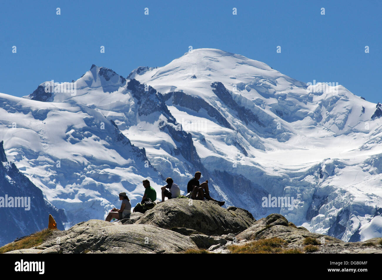 A group of young people at Lac Blanc sat on rocks admiring the views of Mont Blanc Stock Photo