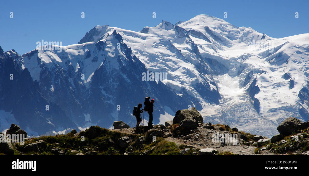 Two women, one carrying a baby in a baby carrier silhouetted against Mont Blanc in the French Alps Stock Photo