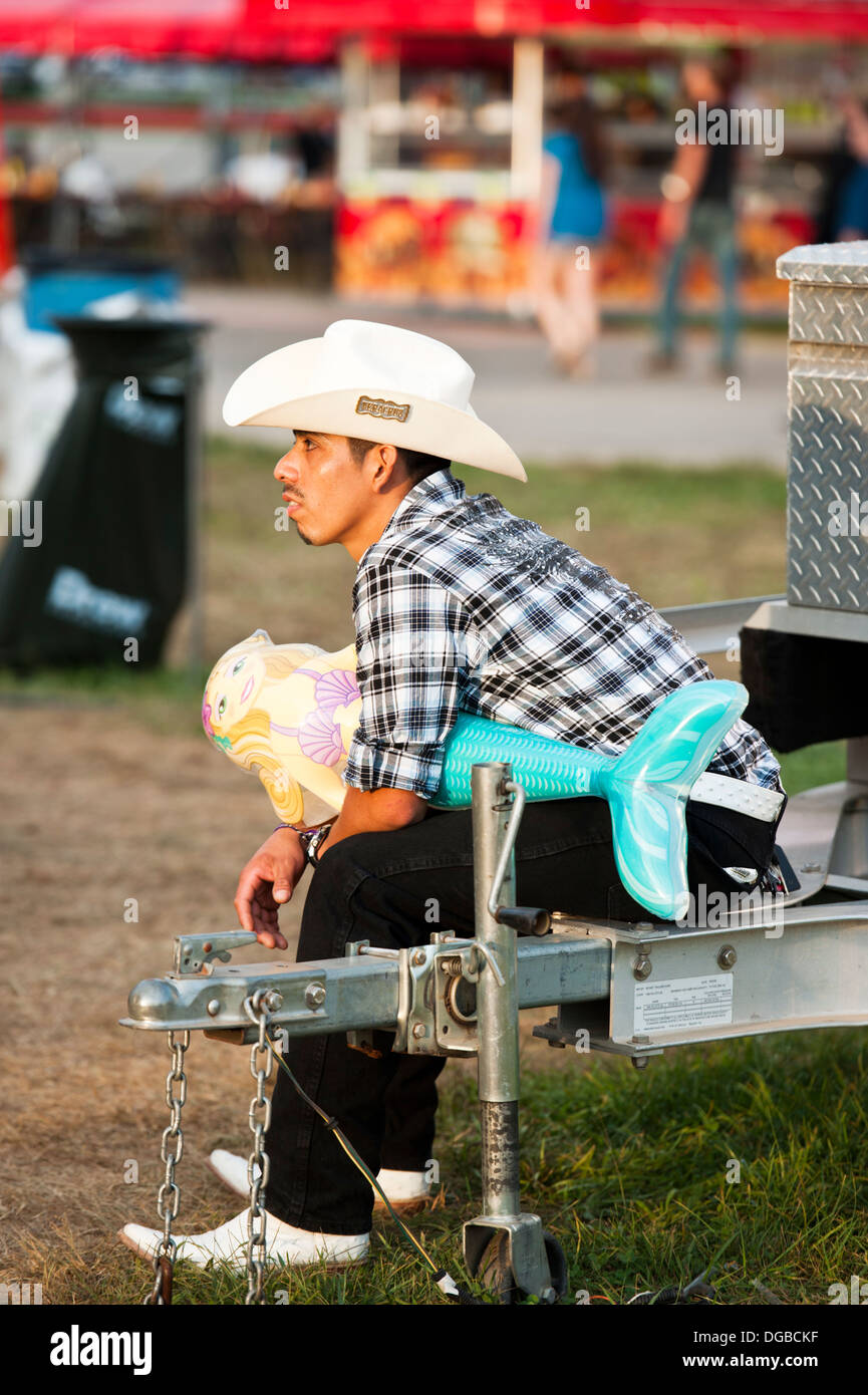 A Latino man wearing boots and cowboy hat holding a carnival prize at the Mountain State Fair in Asheville North Carolina Stock Photo